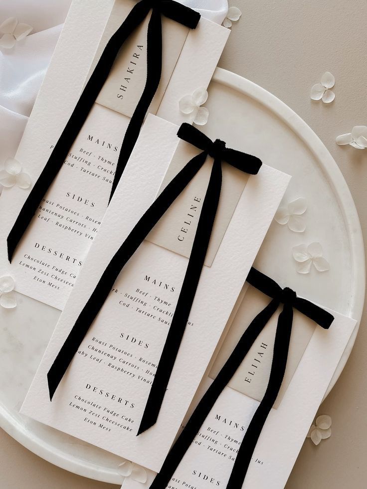 three pieces of paper with black ribbon tied around them on a white plate next to flowers