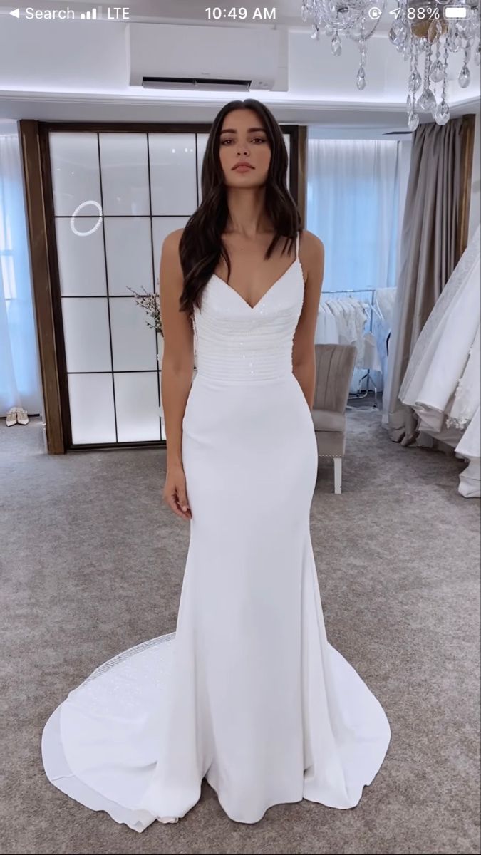 a woman standing in front of a mirror wearing a white wedding dress with spaghetti straps