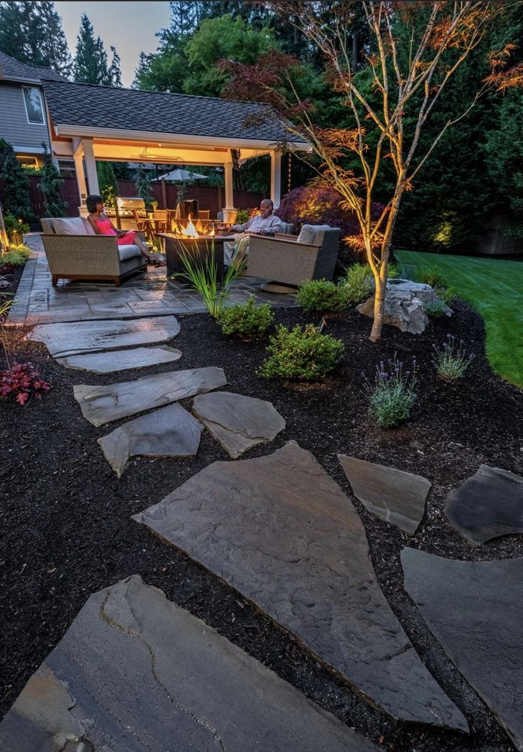 an outdoor patio with stone steps leading to the fire pit and seating area at night