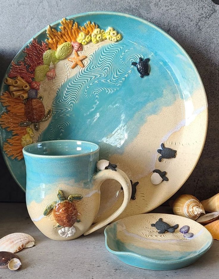 a blue and white ceramic plate with seashells painted on it next to two cups