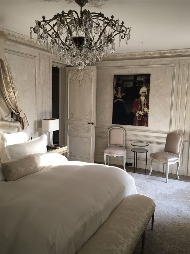 a large white bed sitting in a bedroom next to a chandelier and two chairs