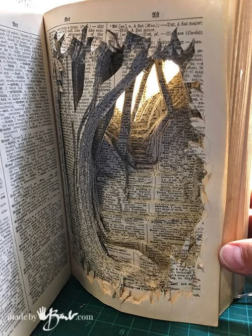 an open book that has been cut into the shape of a face and is being held in