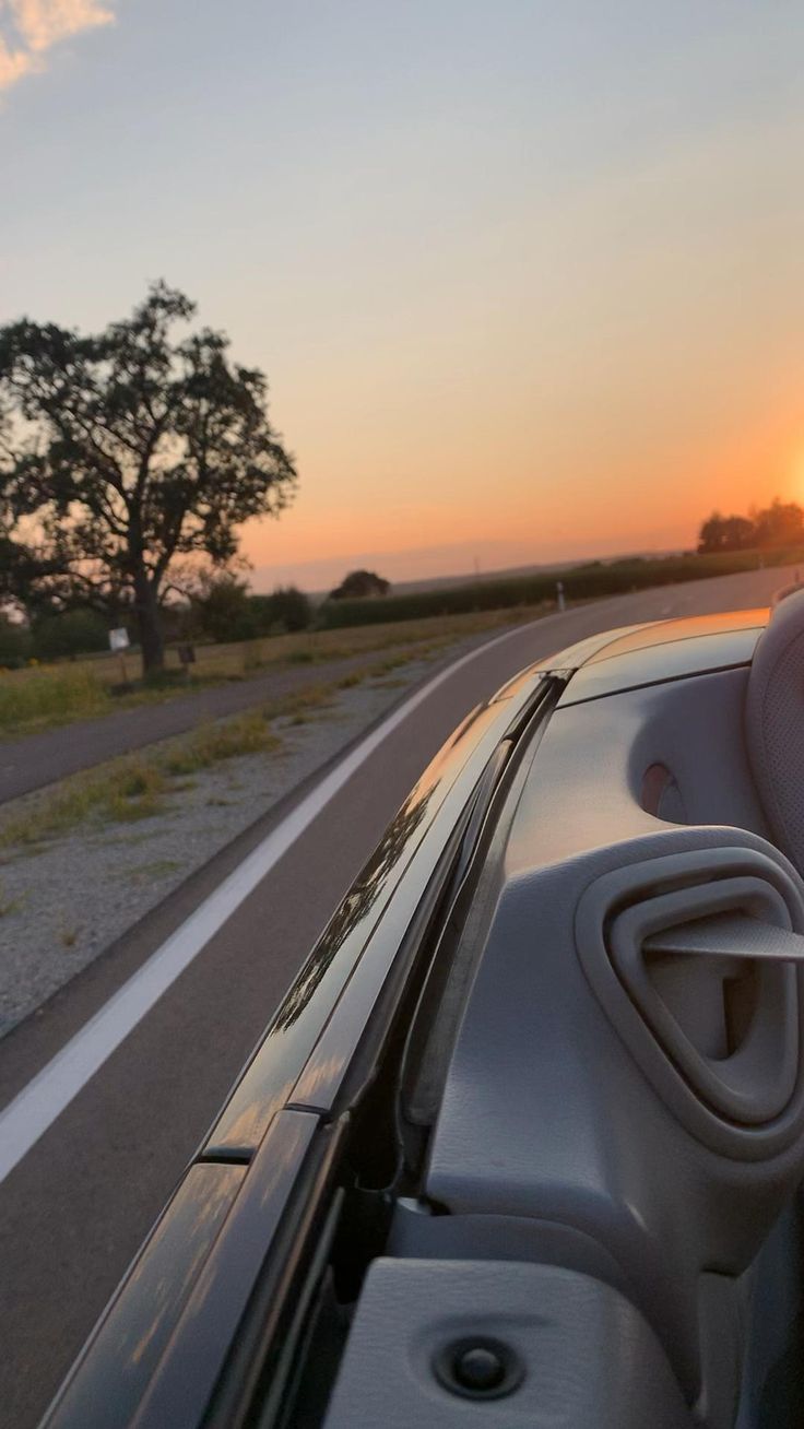 the sun is setting behind an electric car on the road with trees in the background