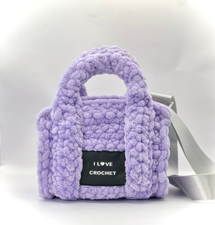 a purple crocheted bag with a white ribbon around the strap and i love crochet tag on it