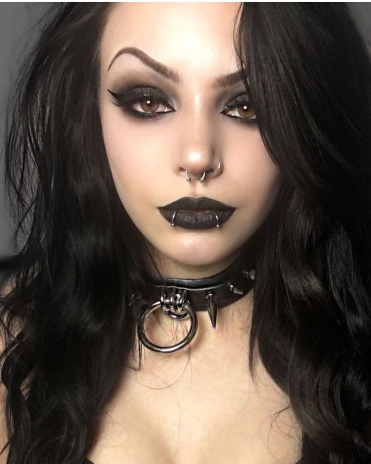 a woman with long black hair wearing a choker and gothic makeup looks at the camera