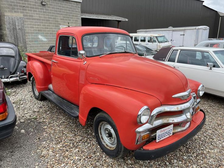 an old red truck is parked in the gravel