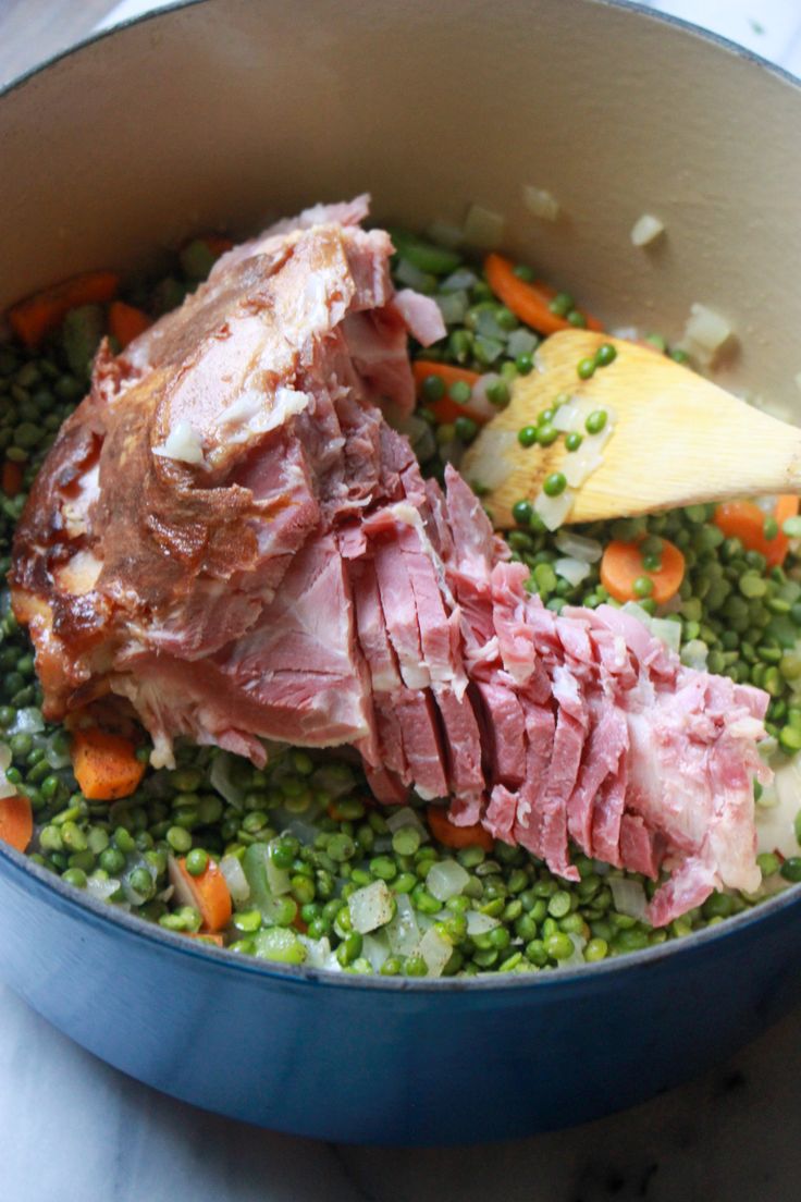 a pot filled with meat and peas on top of a table next to a wooden spoon