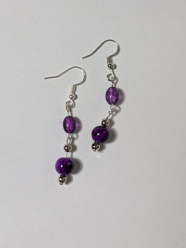 Elevate your jewelry collection with these lovely purple beaded dangling earrings. The round shape and silver tone metal create a chic and sophisticated look, while the hook closure ensures comfortable wear.  Only the best materials are used to create each piece of jewelry  - Glass beads  - Acrylic beads  - Silver tone components Purple Metal Drop Earrings, Elegant Adjustable Purple Beaded Earrings, Purple Drop Crystal Earrings Nickel Free, Nickel Free Purple Crystal Drop Earrings, Purple Metal Dangle Earrings, Purple Dangle Metal Earrings, Purple Drop Earrings With Dangling Beads, Purple Dangle Metal Jewelry, Elegant Purple Crystal Earrings With Dangling Beads