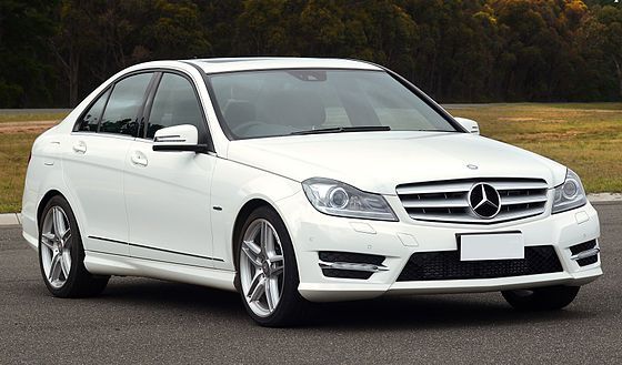 a white mercedes c - class car parked in a parking lot with trees in the background