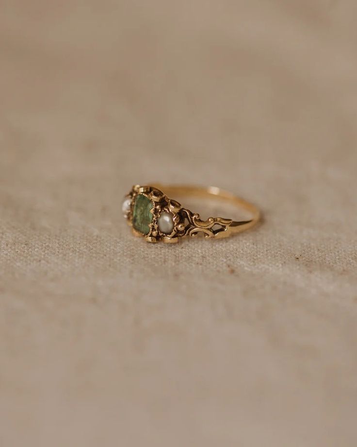 a gold ring with two green stones on the front and one stone in the back