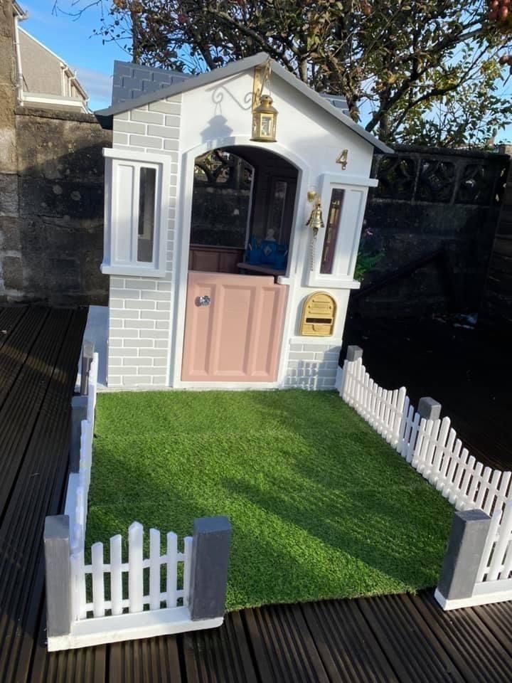 a small white house with a pink door on the front lawn and fence around it