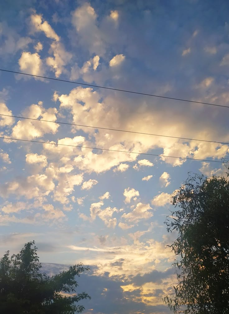 the sky is full of clouds and power lines in the foreground with trees on either side