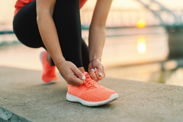 a woman tying her shoelaces on the edge of a concrete wall near water