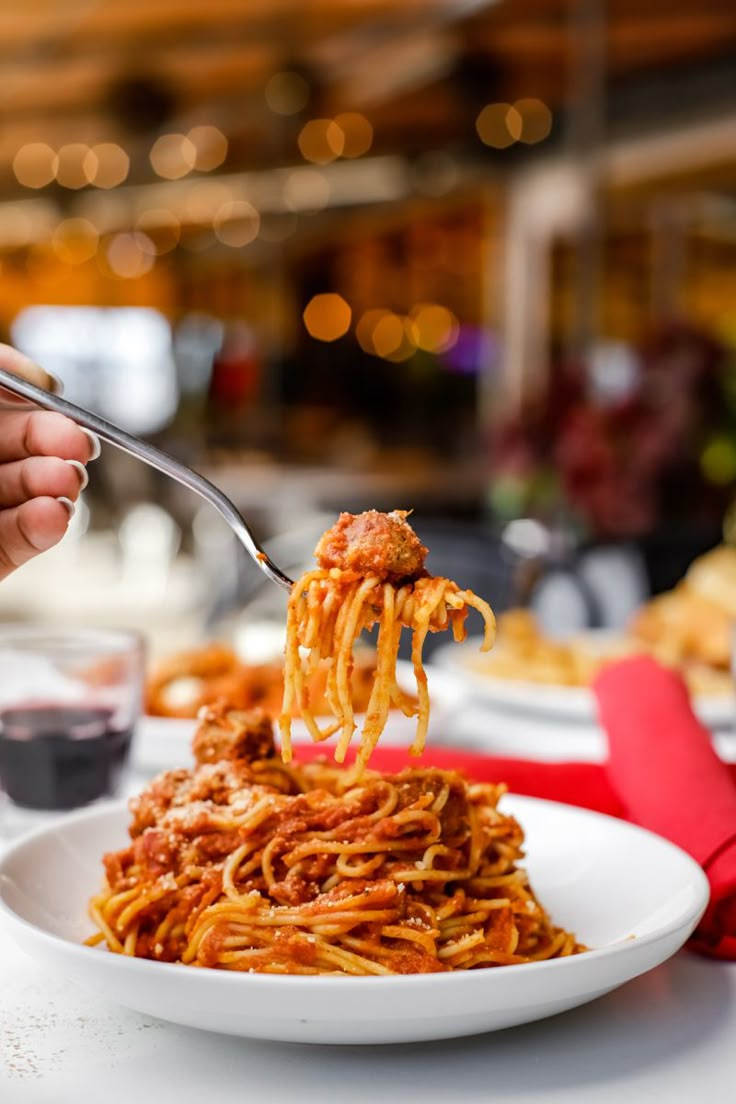 a person holding a fork full of spaghetti on a white plate with red napkins