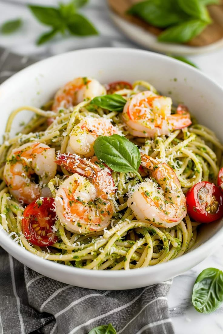 pasta with shrimp and pesto in a white bowl on top of a striped towel