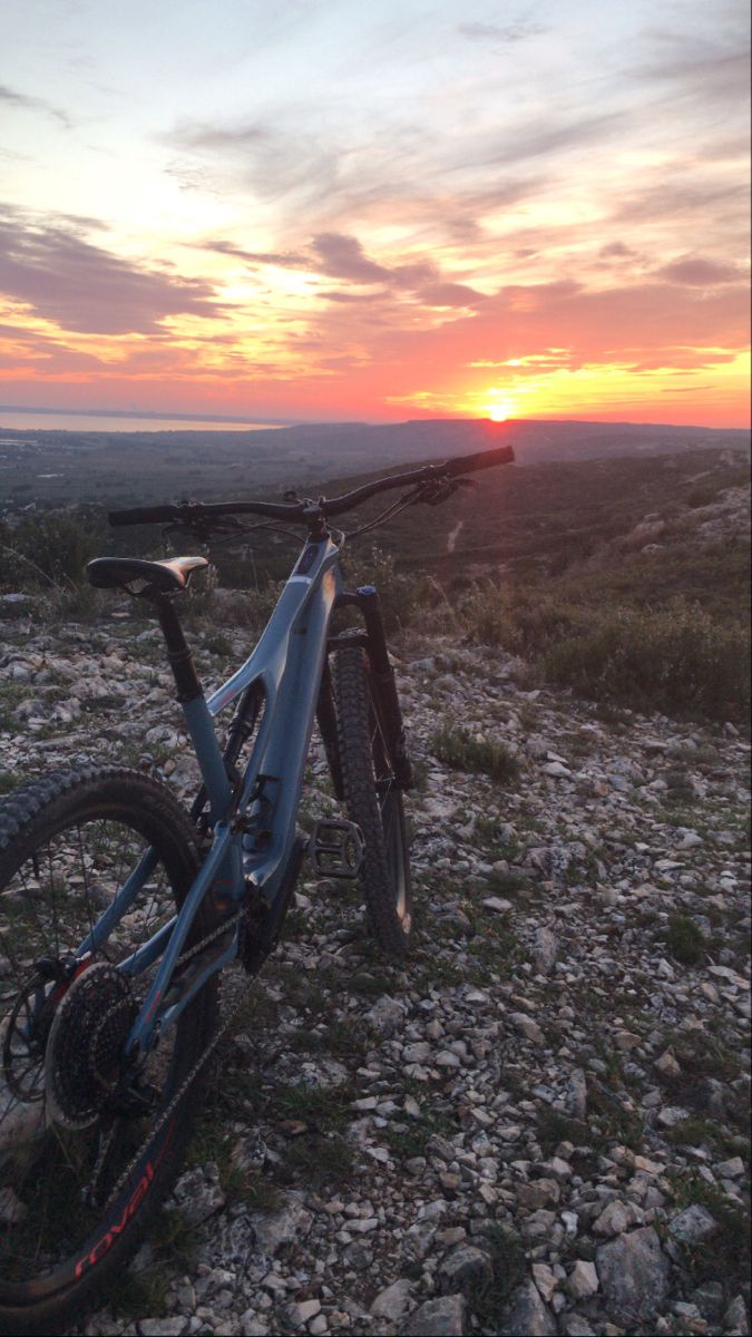 a mountain bike sitting on top of a rocky hillside under a cloudy sky at sunset