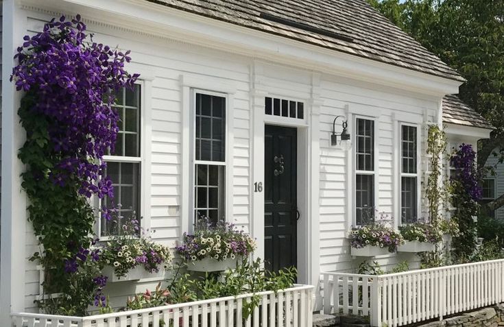 a white house with purple flowers on the windows