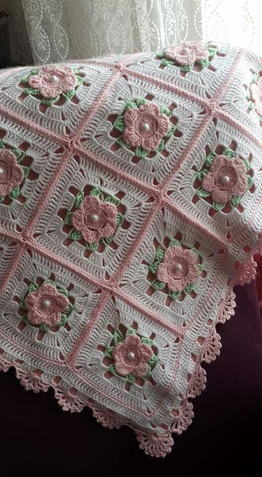 a crocheted blanket with pink flowers on it sitting next to a window sill