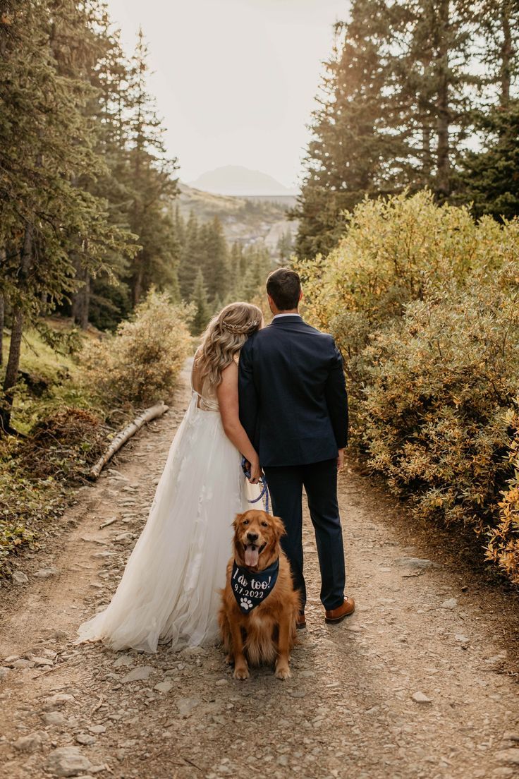 a bride and groom walking their dog down a trail