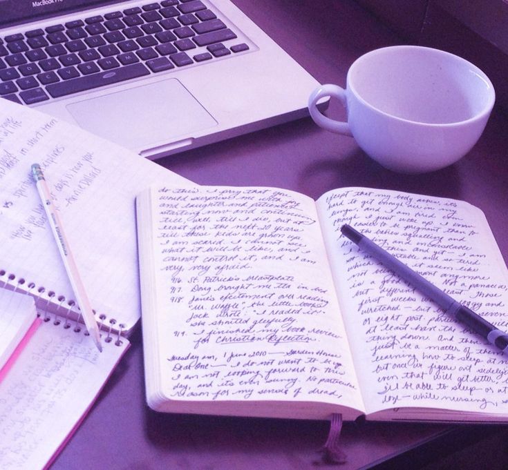 an open notebook sitting on top of a desk next to a cup and laptop computer