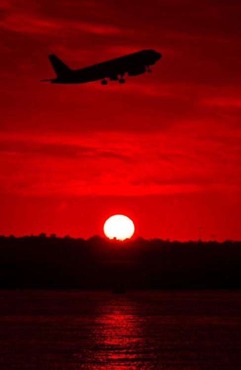 an airplane is flying over the water at sunset