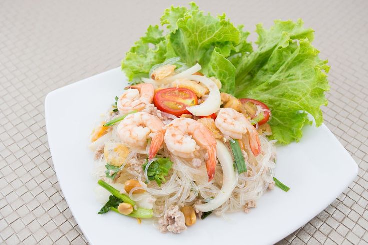 a white plate topped with noodles and shrimp next to lettuce on a table