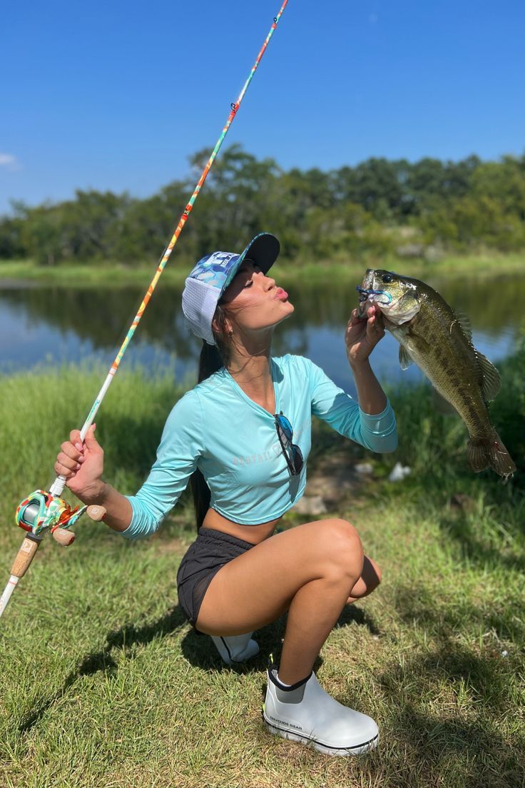 a woman squatting down while holding a fishing rod and a fish in her hand