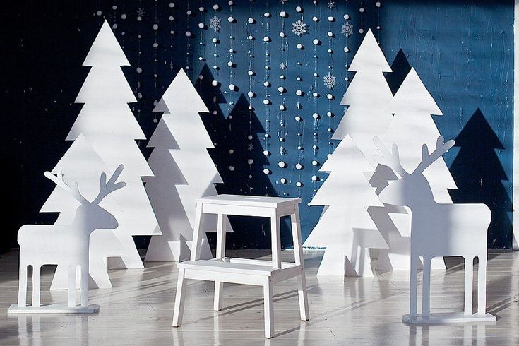 several white paper cut out trees and chairs on a stage with snowflakes in the background