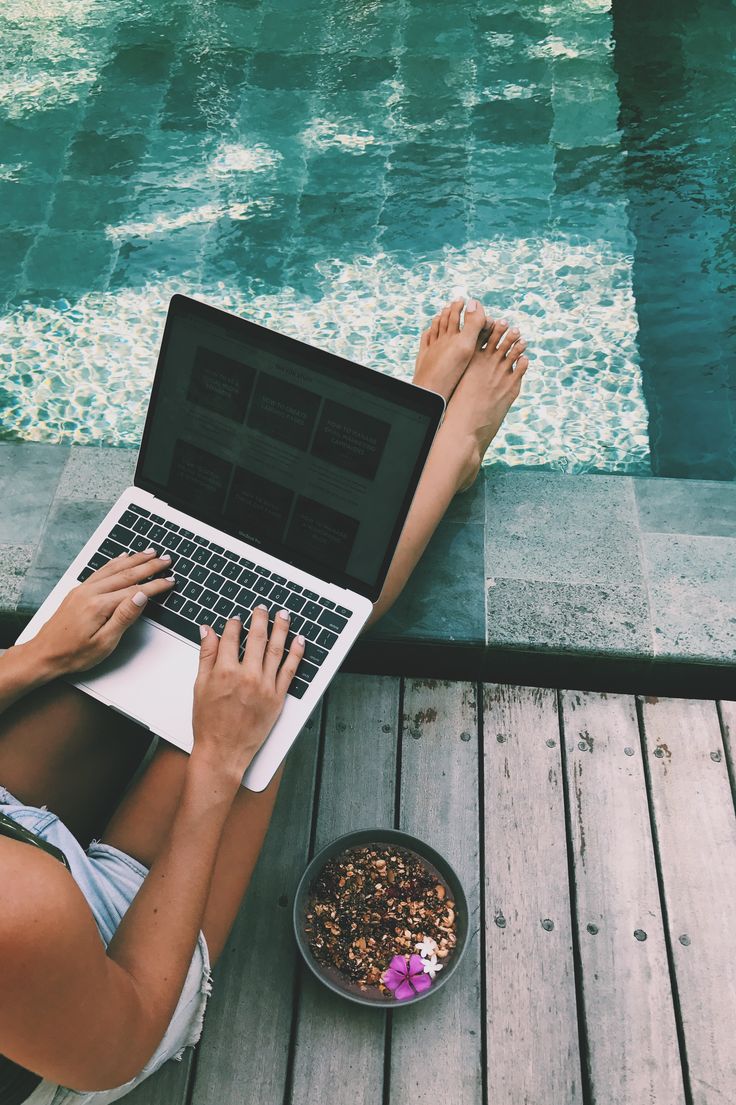 a woman sitting on a dock with her laptop and dog bowl in front of her