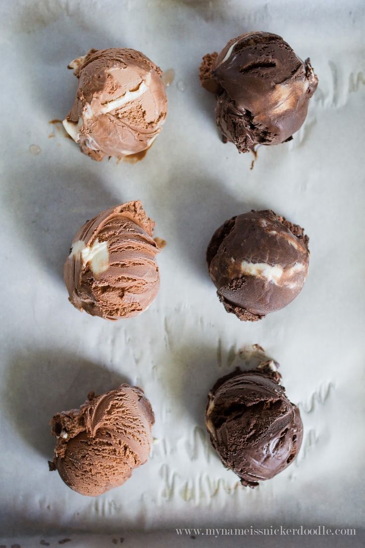 four chocolate ice creams are on a sheet of wax paper and have been frosted