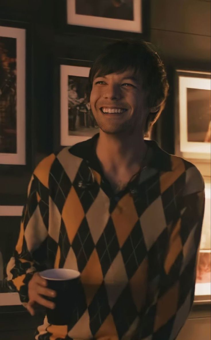 a young man holding a coffee cup in his right hand and smiling at the camera