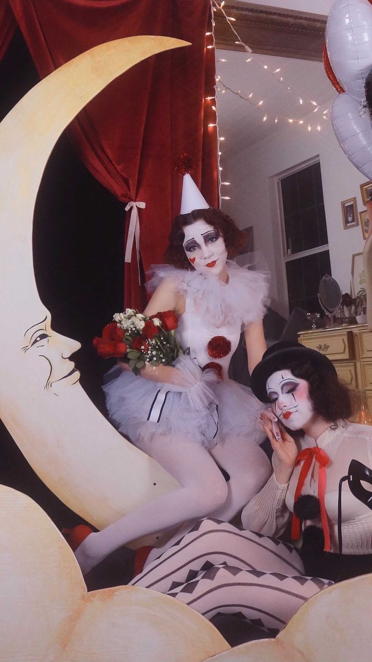 two women dressed in costumes sitting on top of moon shaped objects with balloons around them