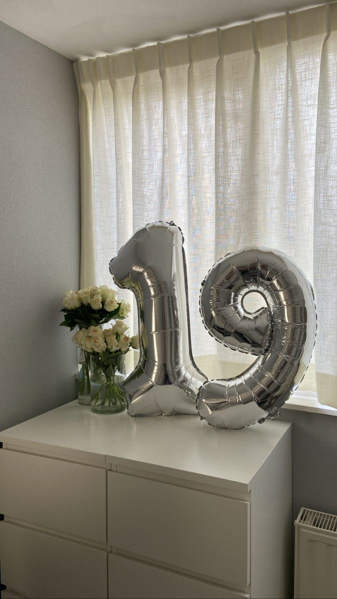 a silver balloon shaped like the number twenty five sitting on top of a white dresser