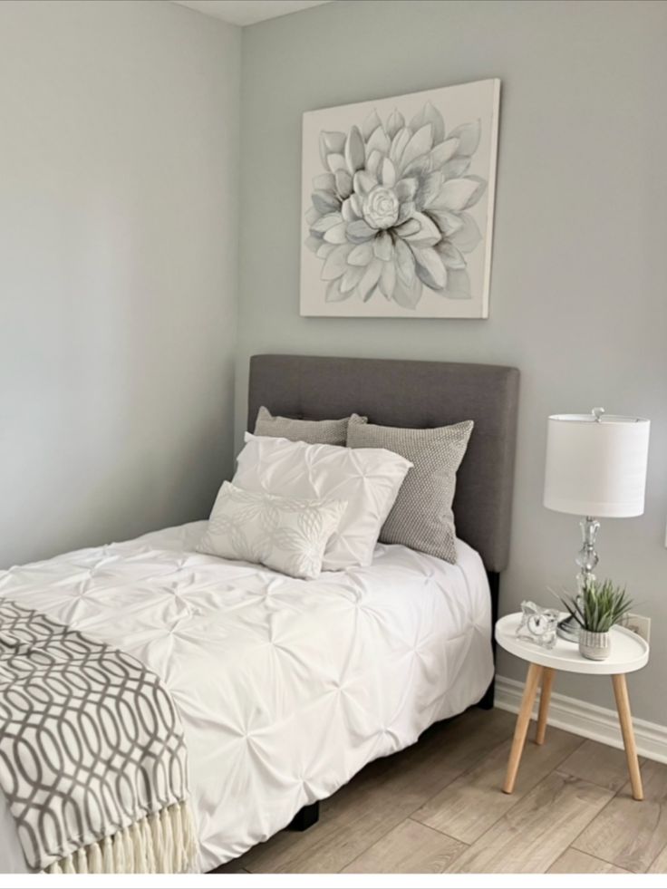 a white bed sitting in a bedroom next to a lamp and painting on the wall