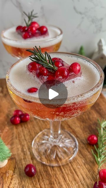 two glasses filled with liquid and cranberries on top of a wooden table