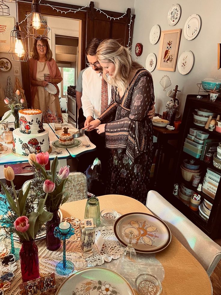 two women standing in a kitchen preparing food on a table with plates and vases