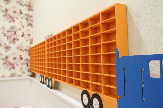 an orange and blue toy truck is next to a wall with shelving on it