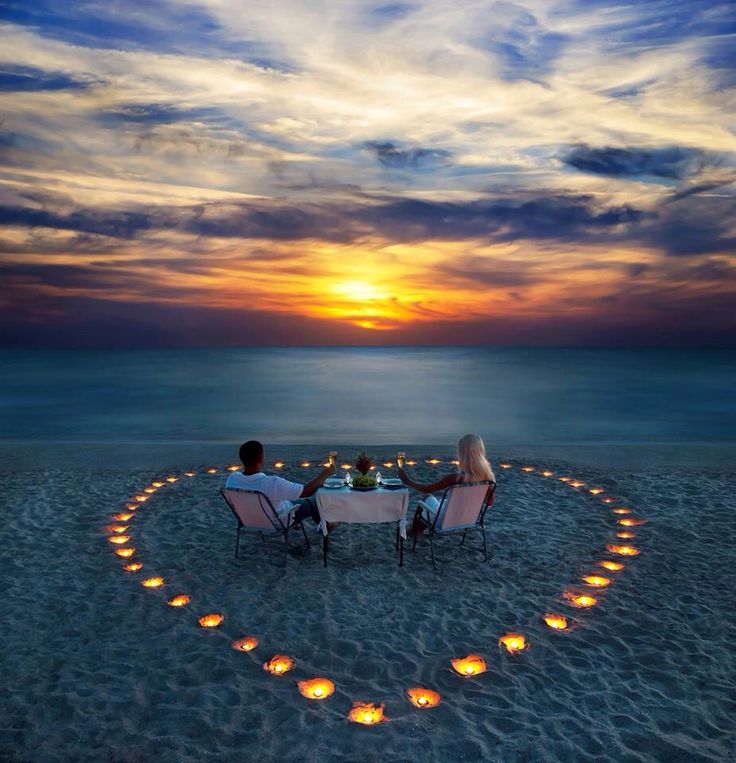 two people sitting at a table in the shape of a heart with candles on it