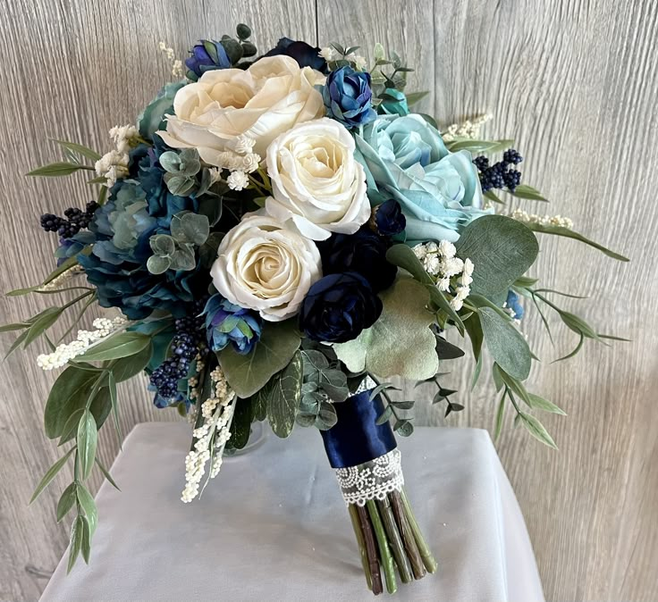 a bridal bouquet with blue, white and green flowers on a tableclothed cloth