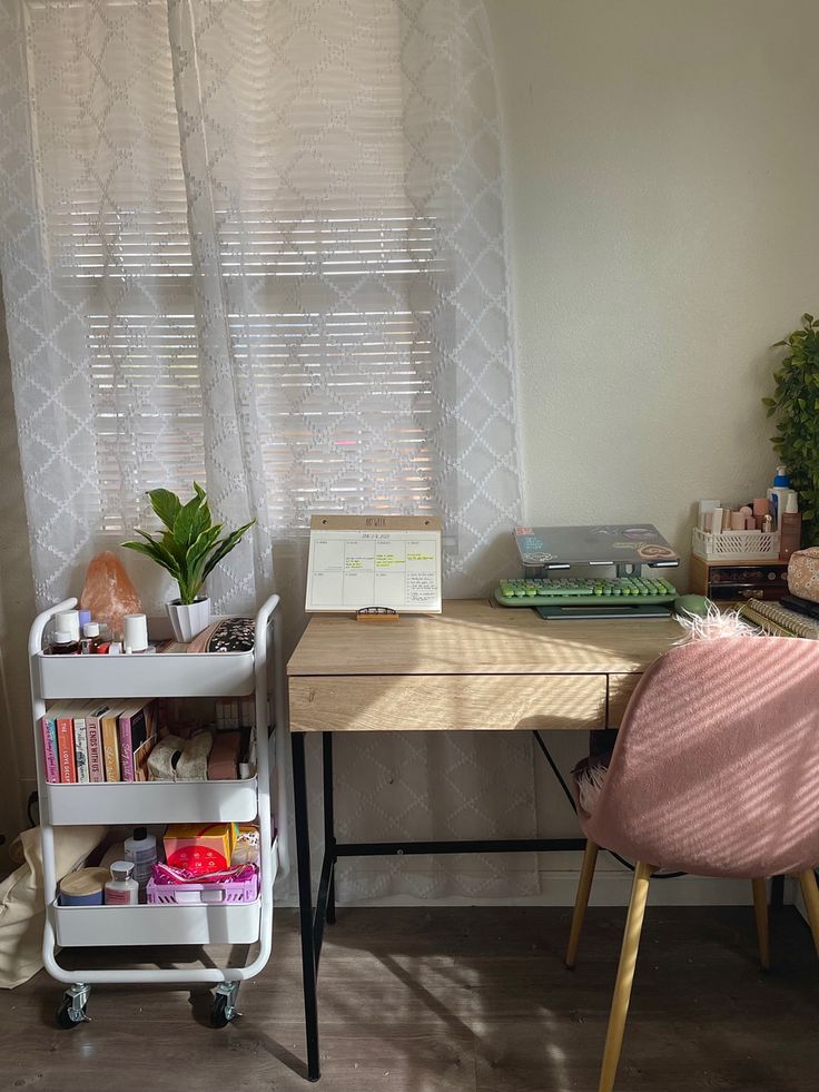 a desk with a laptop and books on it in front of a window covered by sheer curtains