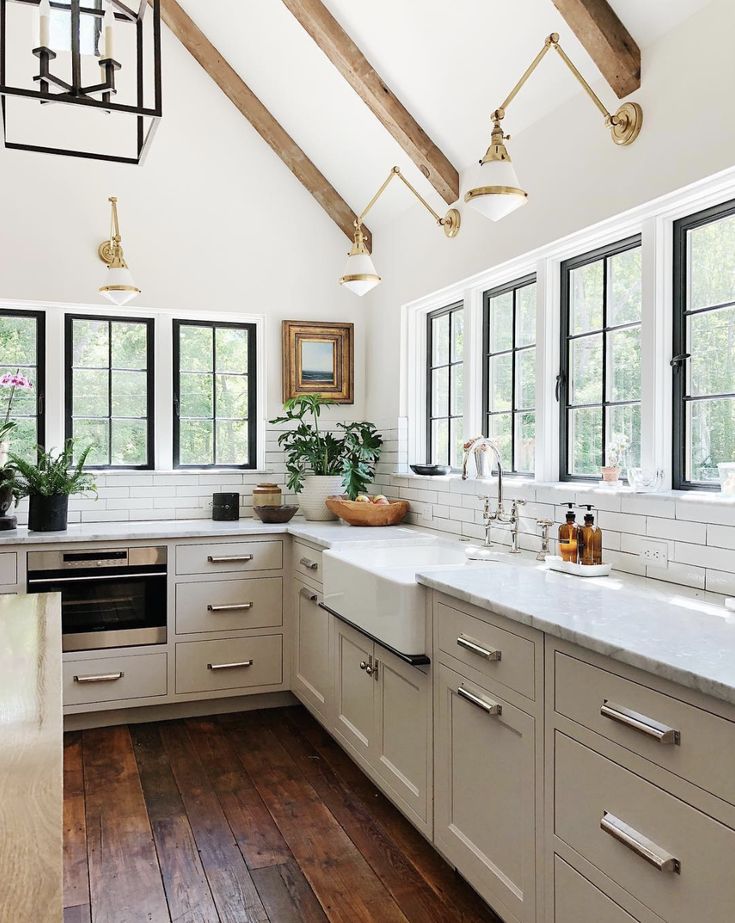 a kitchen with wooden floors and white cabinets, windows, and wood beams on the ceiling