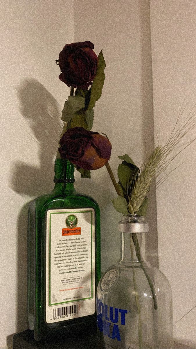 there is a bottle with flowers in it on the shelf next to a glass vase