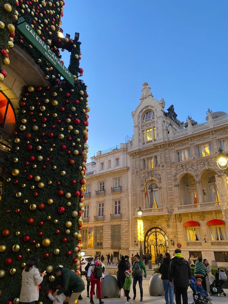 people are standing in front of a christmas tree at the entrance to a large building