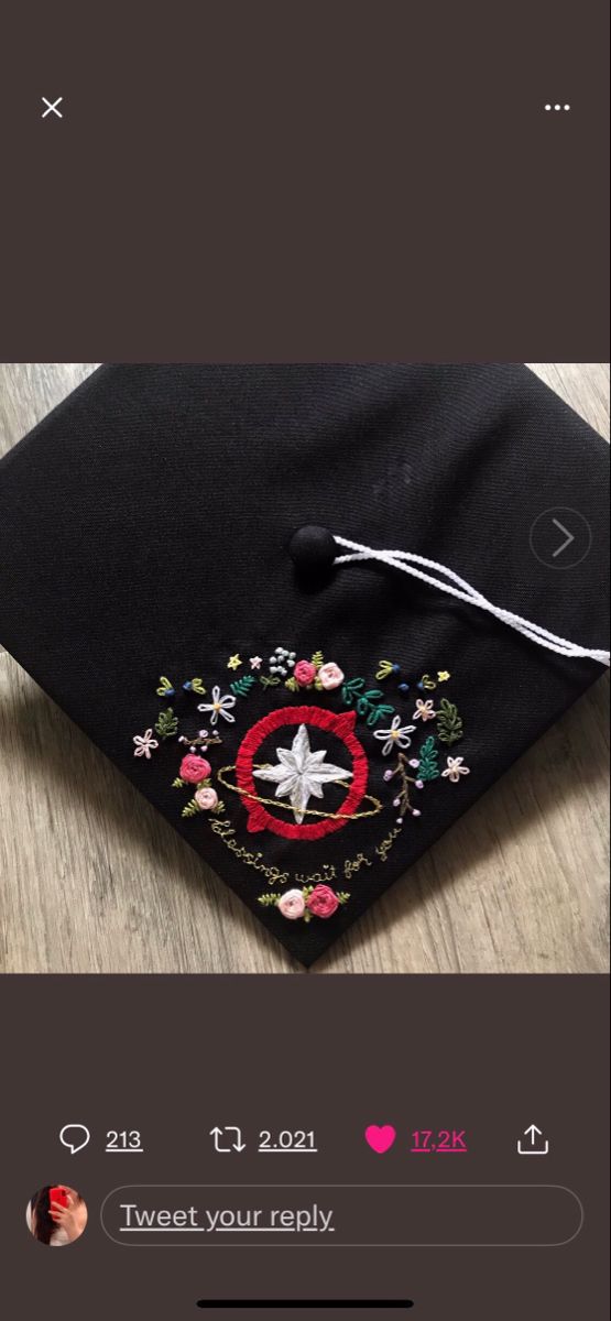 a black graduation cap with embroidered flowers on the front and side, sitting on top of a wooden table