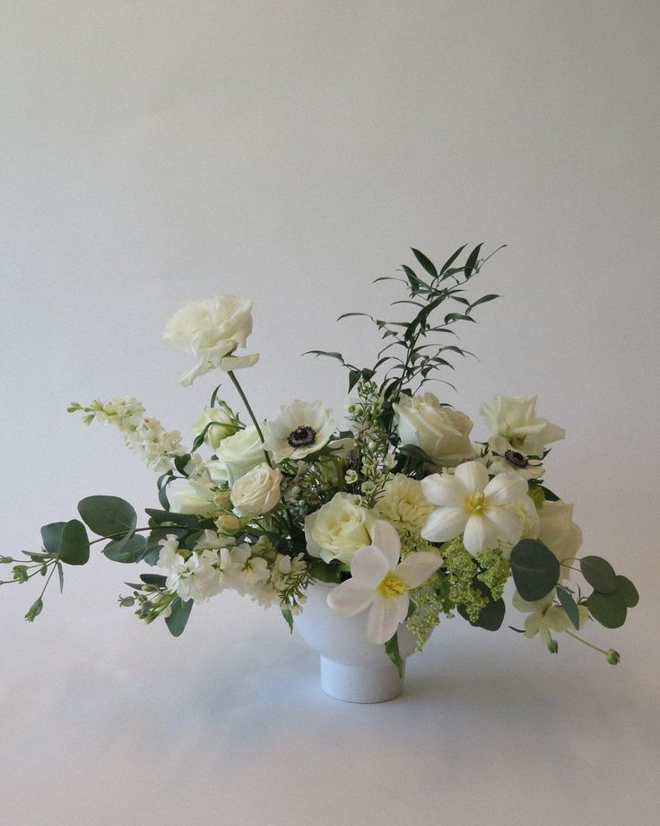 a vase filled with white flowers and greenery