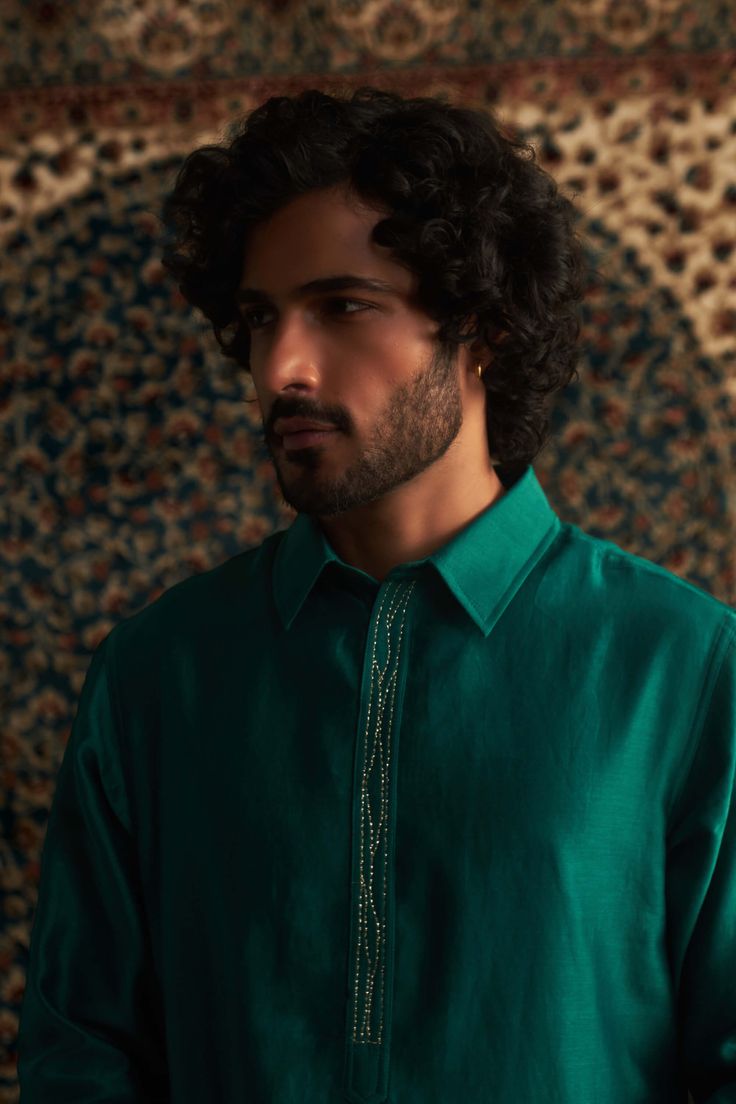 This emerald green pathani kurta set is a stunning choice for festive occasions like mehendi. The subtle embroidery on the placket adds a touch of elegance without being over the top. Paired with a coordinating salwar in a color-on-color design, it strikes the perfect balance between traditional and stylish. This set is sure to become a go-to piece in your wardrobe for celebrating special moments! Green Zari Work Kurta In Cotton Silk, Green Cotton Silk Kurta With Zari Work, Traditional Green Sherwani With Mirror Work, Green Kurta With Naqshi And Traditional Drape, Green Kurta With Naqshi In Traditional Drape, Long Sleeve Kurta With Mirror Work For Eid, Green Kurta With Dabka Work In Cotton Silk, Green Kurta With Mirror Work And Traditional Drape, Green Cotton Silk Kurta With Dabka Work