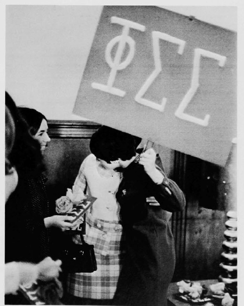 a woman holding a sign that says pizz in front of other women standing around