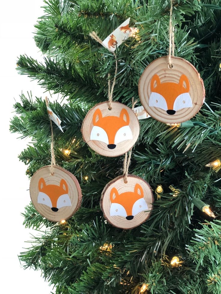 three wooden ornaments hanging from a christmas tree with lights around them and a fox face on the front