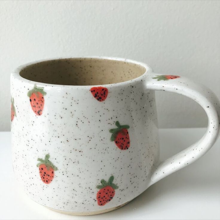 a coffee cup with strawberries on it sitting on a white counter top next to a wall