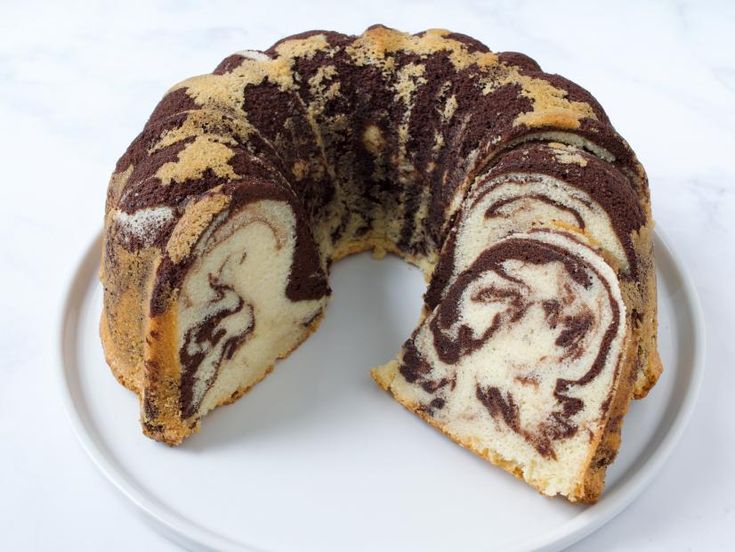 a chocolate swirl bunt cake on a white plate with one slice cut out and ready to be eaten